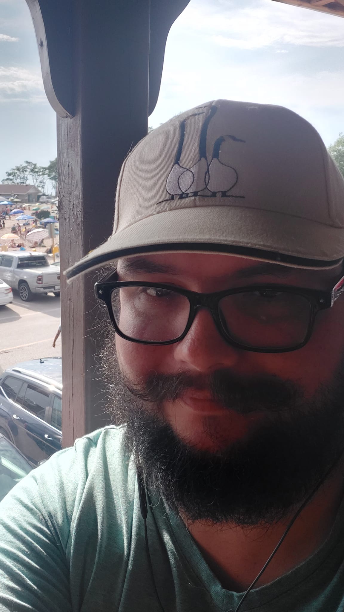 A man with short hair and bushy facial hair sits on a second floor patio overlooking a busy beach